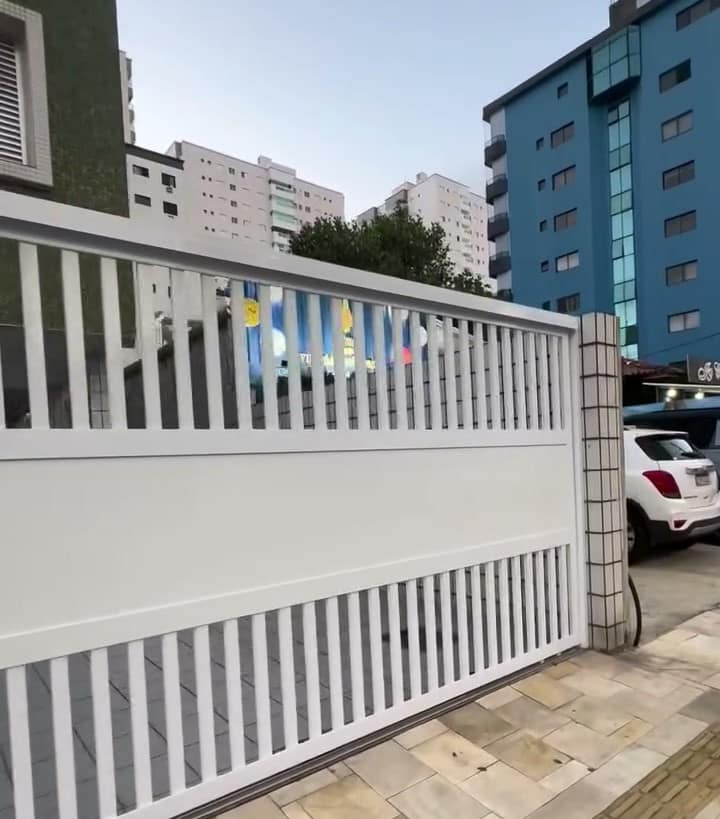 Portão branco e muro de uma casa com os prédios atrás