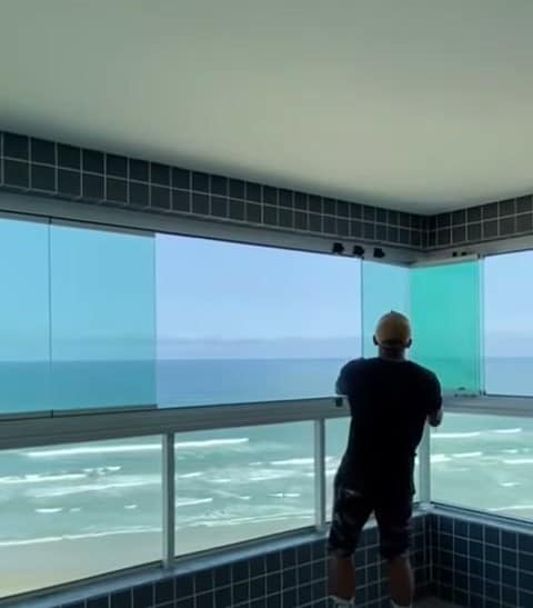 Sacada envidraçada de frente para o mar, com o vidro fechado e a praia ao fundo