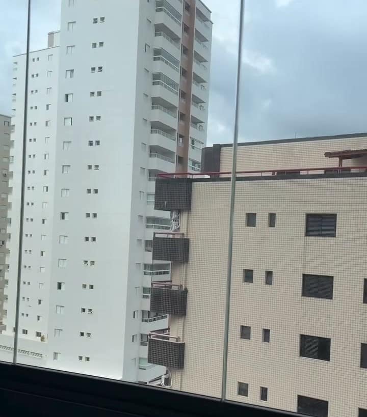 Sacada envidraçada com guarda-corpo de vidro e vista para os prédios
