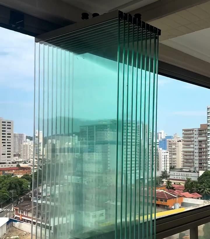 Painéis de vidro abertos numa sacada ampla com vista para os prédios